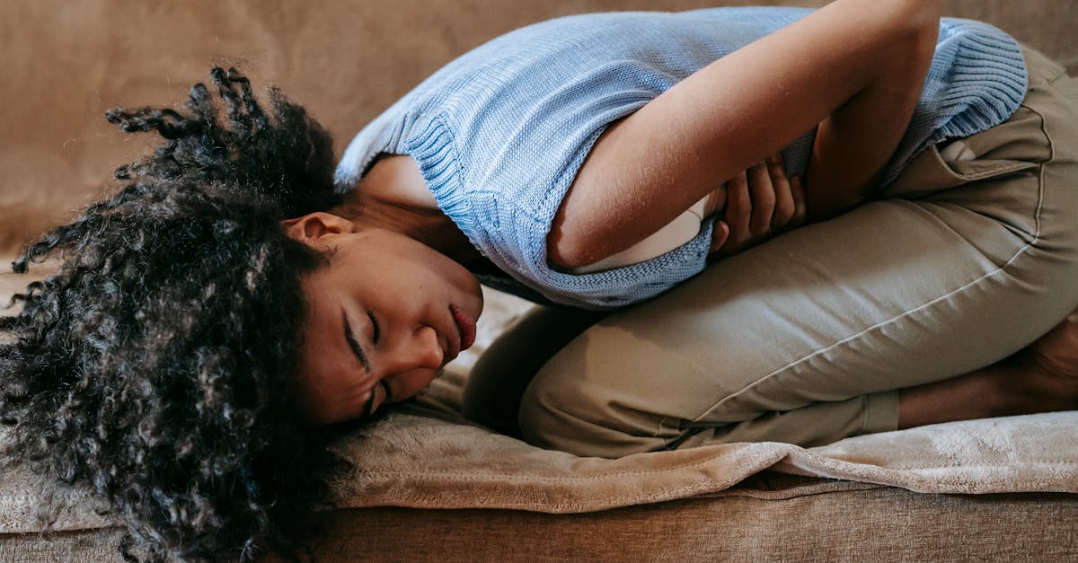 Side view of young African American female in agony on couch while having pain in stomach